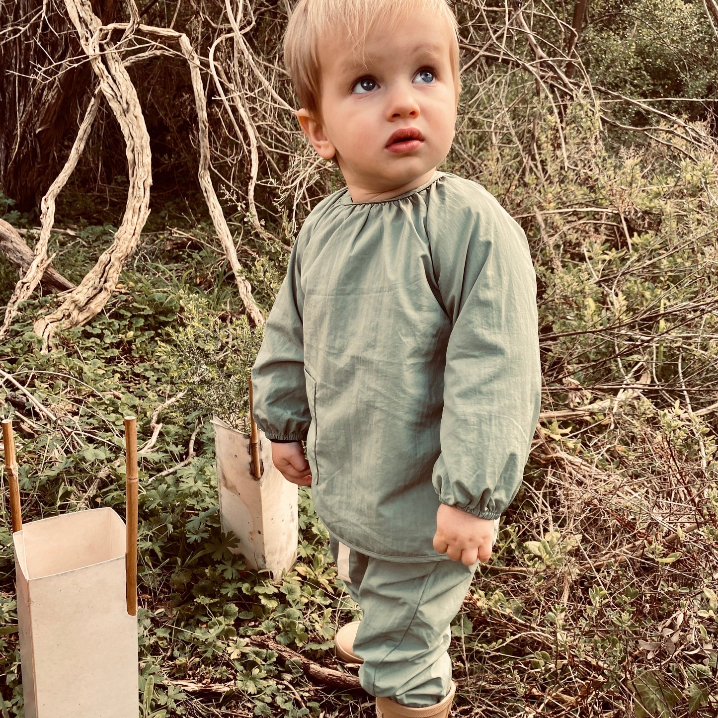 boy exploring the bush in his rain pants and messy smock. keeping clean, dry and protected in his sustainable, water resistant clothing